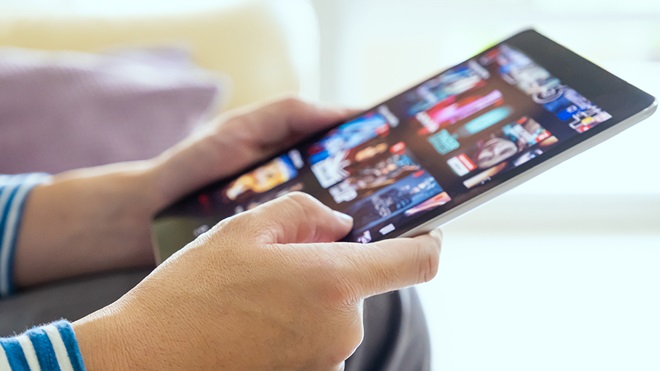 hands holding a tablet with a movie streaming service on the screen