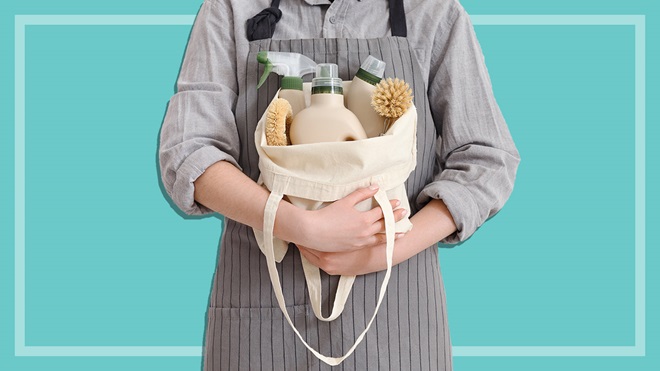 person wearing apron and holding bag of green cleaning products and brushes
