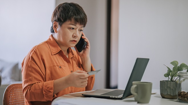 person on phone to bank while holding credit card and looking at laptop