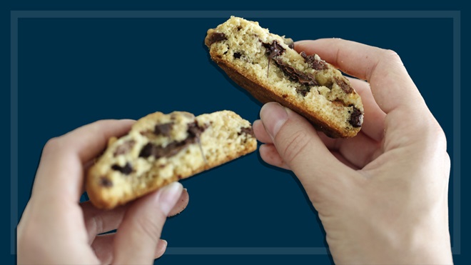 hands holding a chocolate chip cookie broken in half