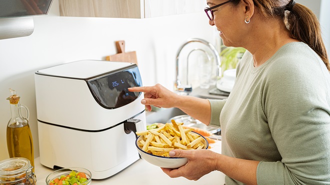 person putting large bowl of chips into air fryer